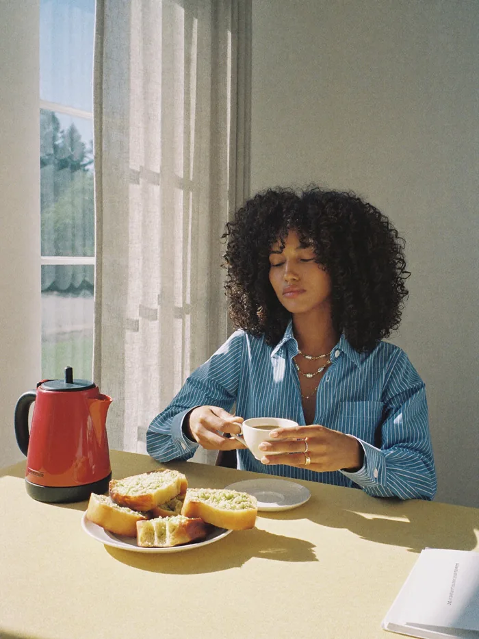 Mujer tomando café en la cocina con una pava roja