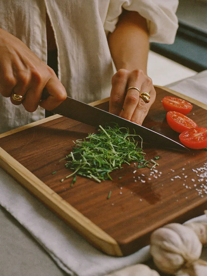 Manos cortando hierbas y tomates sobre una tabla de madera