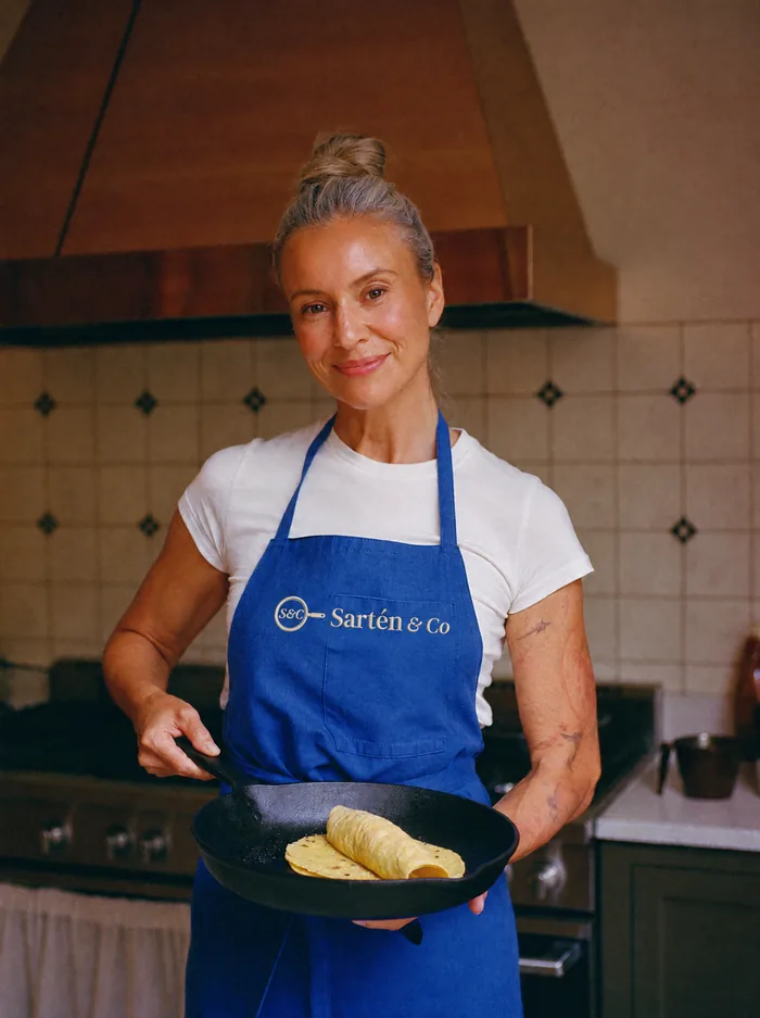 Mujer con delantal azul sosteniendo una sartén de hierro con una tortilla